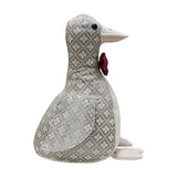 Duck-shaped door stop in grey and off-white jacquard floret pattern, with cream suede-feel beak, front and feet, a red bow tie at the neck, and black bead eyes, shown against a plain white background.