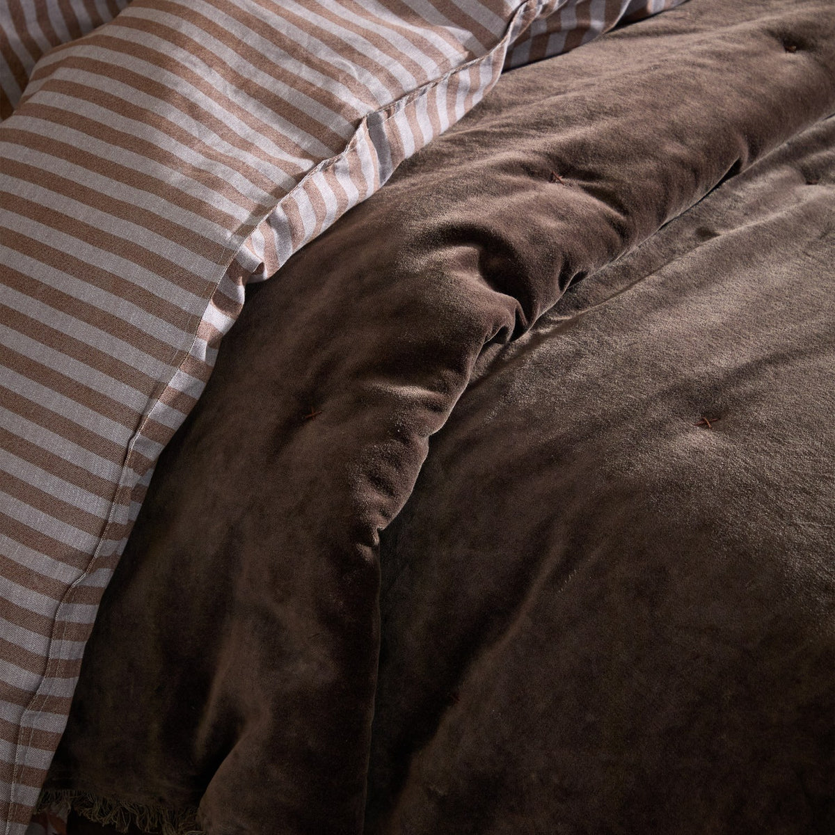 Jaye Velvet Cotton Bedspread in Bitter Chocolate, close-up of tufted brown velvet quilting beside a beige and white striped pillowcase.