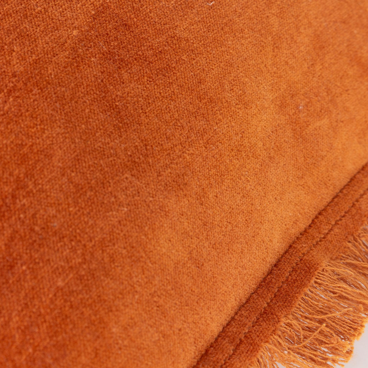 Close-up of the Jaye Velvet Cotton Cushion in rust, showing the plain velvet pile texture and a fringed trim edge with double-stitched seam.