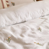 Josephine Cotton Floral Duvet Cover Set in white, showing crinkled cotton muslin fabric with small embroidered peach and green floral stems, styled with a matching pillow on a bed.