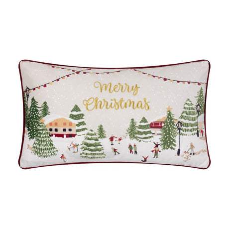 Cream rectangular cushion embroidered with a snowy village scene, festive trees and figures, gold Merry Christmas text, and a berry red piped edge.