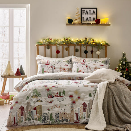 Joy To All duvet cover set on a bed, featuring a festive cityscape print with skyscrapers, a big wheel, cable cars and a sleigh in cream, grey, red and green, with matching pillowcases.