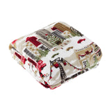 Folded Joy To All printed polyester throw in cream, featuring a festive scene of city buildings, trees, cable cars and taxis in red, green and brown, shown on a plain white background.