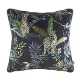 Square velvet cushion with a hand-painted jungle print of two leopards, banana leaves, ferns and a toucan on a dark ground, with petrol-toned piping, shown on a white background.