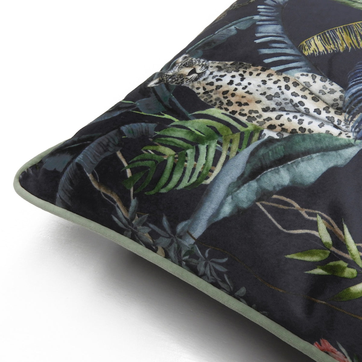 Square velvet cushion, corner view, with a hand-painted jungle scene of a leopard among palm leaves and ferns on a dark ground, edged with petrol-green piping.