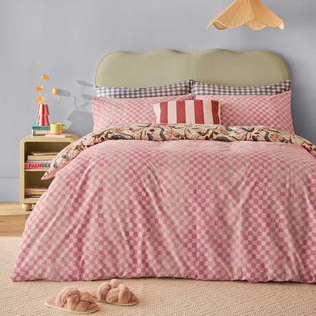 Juno Reversible Check Duvet Cover Set on a bed in pink and cream check with floral reverse trim, styled with striped and gingham cushions in a bedroom setting.