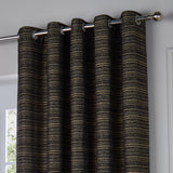 Jupiter Chenille Fully Lined Eyelet Curtain in black with fine gold horizontal striping, shown hung on a chrome pole with eyelet header in a bright room.