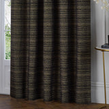 Black and gold Jupiter chenille fully lined eyelet curtains with horizontal gold threading, hanging beside a French door and side table in a living room.