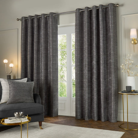 Jupiter Chenille Fully Lined Eyelet Curtains in graphite, shown as a floor-length pair with eyelet header on a chrome pole, framing a glazed door in a living room setting.