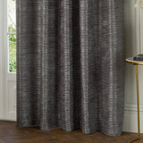 Jupiter Chenille Fully Lined Eyelet Curtains in graphite, showing a textured woven fabric with fine horizontal lines, hung beside a window in a living room setting.