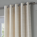 Jupiter Chenille Fully Lined Eyelet Curtains in ivory/gold, showing chrome eyelet rings on a metal pole with a fine horizontal woven texture, hung by a window.