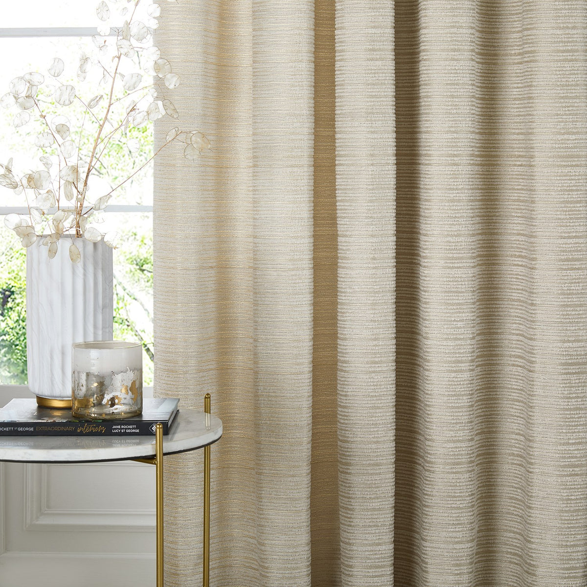 Jupiter Chenille Fully Lined Eyelet Curtains in ivory/gold, showing fine horizontal woven texture, styled with soft folds beside a window in a living room setting.