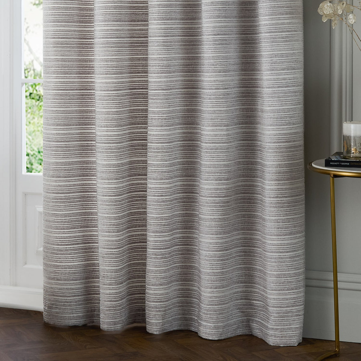 Jupiter Chenille Fully Lined Eyelet Curtains in silver, hung in soft folds beside a window, showing fine horizontal woven texture and eyelet header detail.