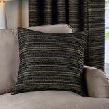 Jupiter Jacquard Chenille Cushion in black with fine gold horizontal stripes, styled on a taupe armchair against a matching striped curtain in a living room setting.