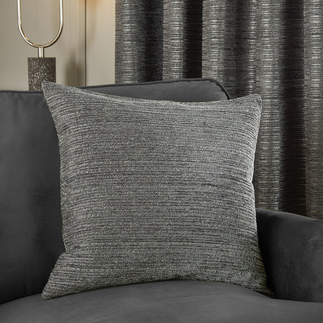 Jupiter Jacquard Chenille Cushion in graphite grey with ridged horizontal texture, styled on a dark grey sofa against striped charcoal curtains.