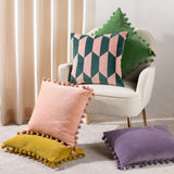 Kalho Jacquard Velvet Cushion in pink and green geometric pattern, styled on a cream armchair with pink, yellow, and purple pom-pom trim cushions nearby.