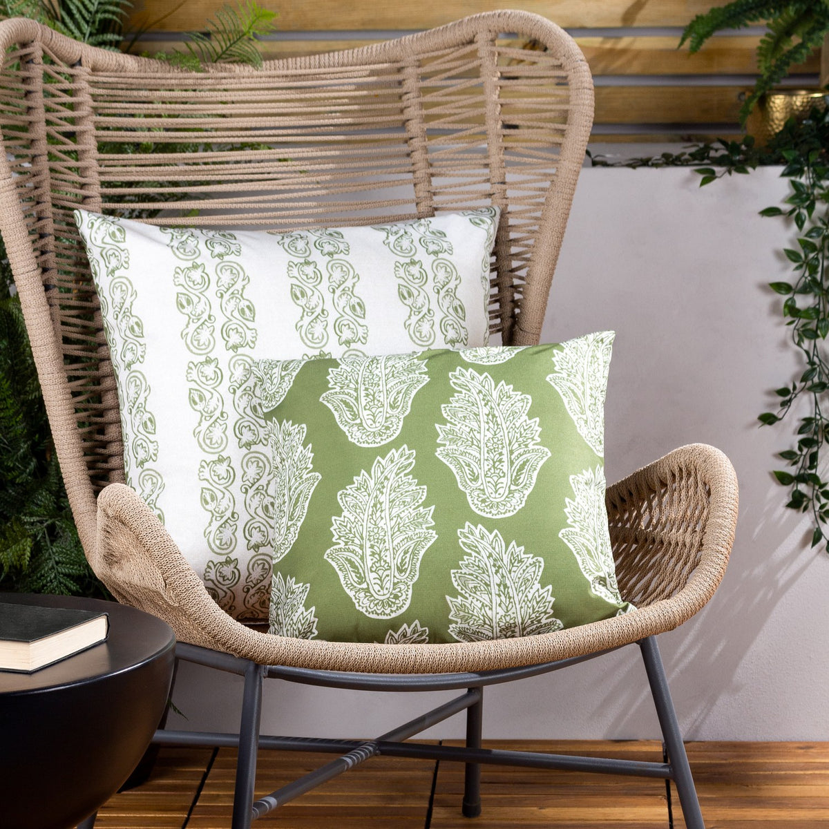 Kalindi reversible polyester cushions in olive, showing paisley print in white-on-olive and olive-on-white, styled on a woven rattan chair.