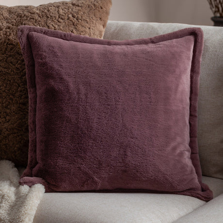Kallu Reversible Faux Fur Cushion in mulberry with an Oxford flange border, shown on a light grey sofa alongside a brown textured cushion and cream throw.