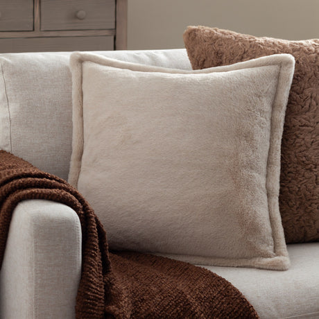 Kallu Reversible Faux Fur Cushion in natural beige with Oxford flange edge, shown on a light sofa beside a brown textured cushion and throw.