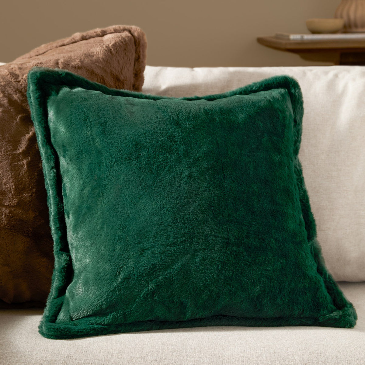 Kallu Plain Faux Fur Cushion in needle green, square with a raised border and plush pile, shown on a sofa beside a brown textured cushion.