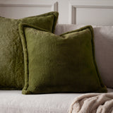 Kallu Reversible Faux Fur Cushions in olive green, square with plain sides and a plush pile, shown on a light grey sofa beside a beige throw.