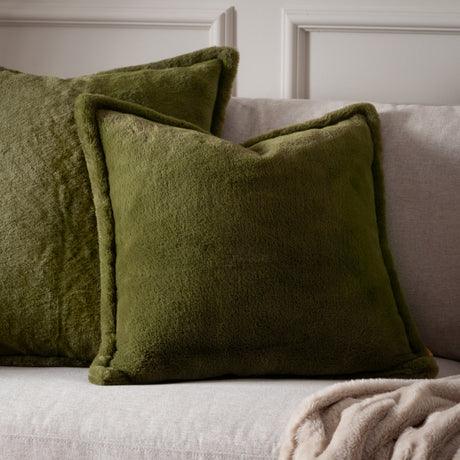 Kallu Reversible Faux Fur Cushions in olive green, square with plain sides and a plush pile, shown on a light grey sofa beside a beige throw.