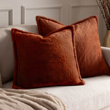 Two square Kallu reversible faux fur cushions in rust orange with a dense plush pile, shown on a light beige sofa in a living room setting.