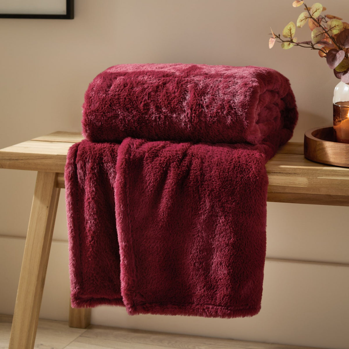Kallu Polyester Throw in berry-red faux fur, folded with a plush pile, draped over a wooden bench in a living room setting.