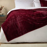 Kallu Polyester Throw in Berry, a deep red faux fur-style throw with a dense plush pile, draped over a white bed beside white pillows in a bedroom setting.