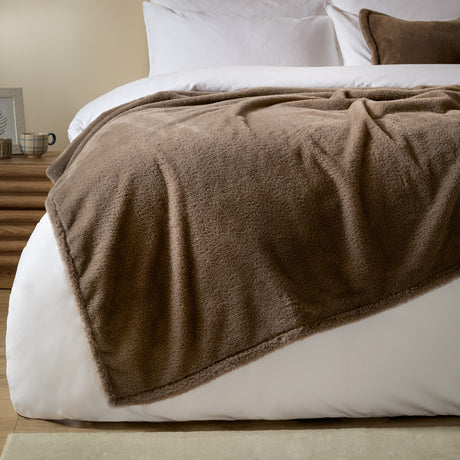 Kallu Reversible Faux Fur Throw in mocha brown draped over a white bed, showing its soft double-sided pile texture in a bedroom setting.