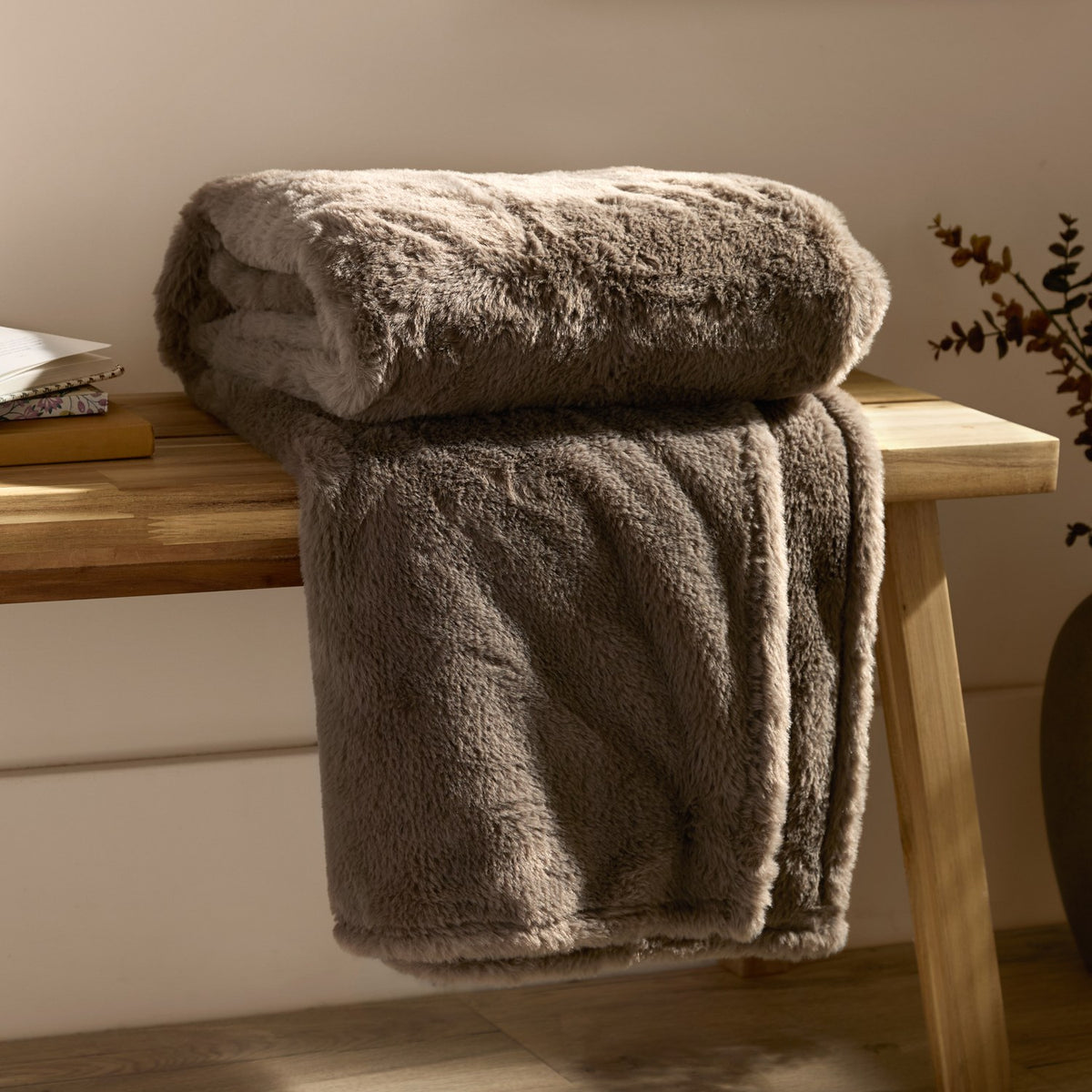 Kallu Reversible Faux Fur Throw in mocha, folded and draped over a wooden bench, showing a soft, textured double-sided pile in a warm brown tone.