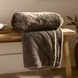 Kallu Reversible Faux Fur Throw in mocha, folded and draped over a wooden bench, showing a soft, textured double-sided pile in a warm brown tone.