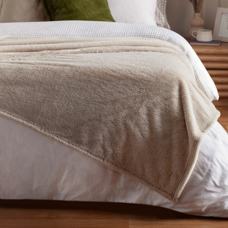 Kallu Reversible Faux Fur Throw in natural draped over a white bed, showing its soft double-sided texture and folded edge detail in a bedroom setting.