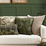 Kielder Forest Woodland Velvet Cushion in khaki green with a fern print, shown on a cream sofa alongside patterned and textured cushions.