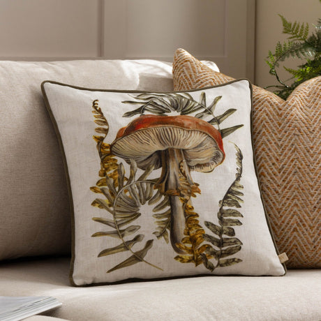 Kielder Forest Mushroom Velvet Cushion in Natural, cream fabric front with hand-painted rust mushroom and olive fern design, shown on a beige sofa.