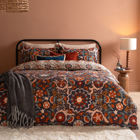 Kinfolk Reversible Floral Duvet Cover Set in Denim Blue with rust, orange and cream medallion print, styled on a bed with matching pillowcases in a warm-toned bedroom.
