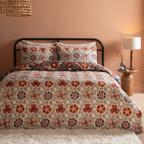 Kinfolk Reversible Floral Duvet Cover Set in denim blue with rust, orange and cream floral medallion print, styled on a bed with matching pillowcases in a warm-toned bedroom.