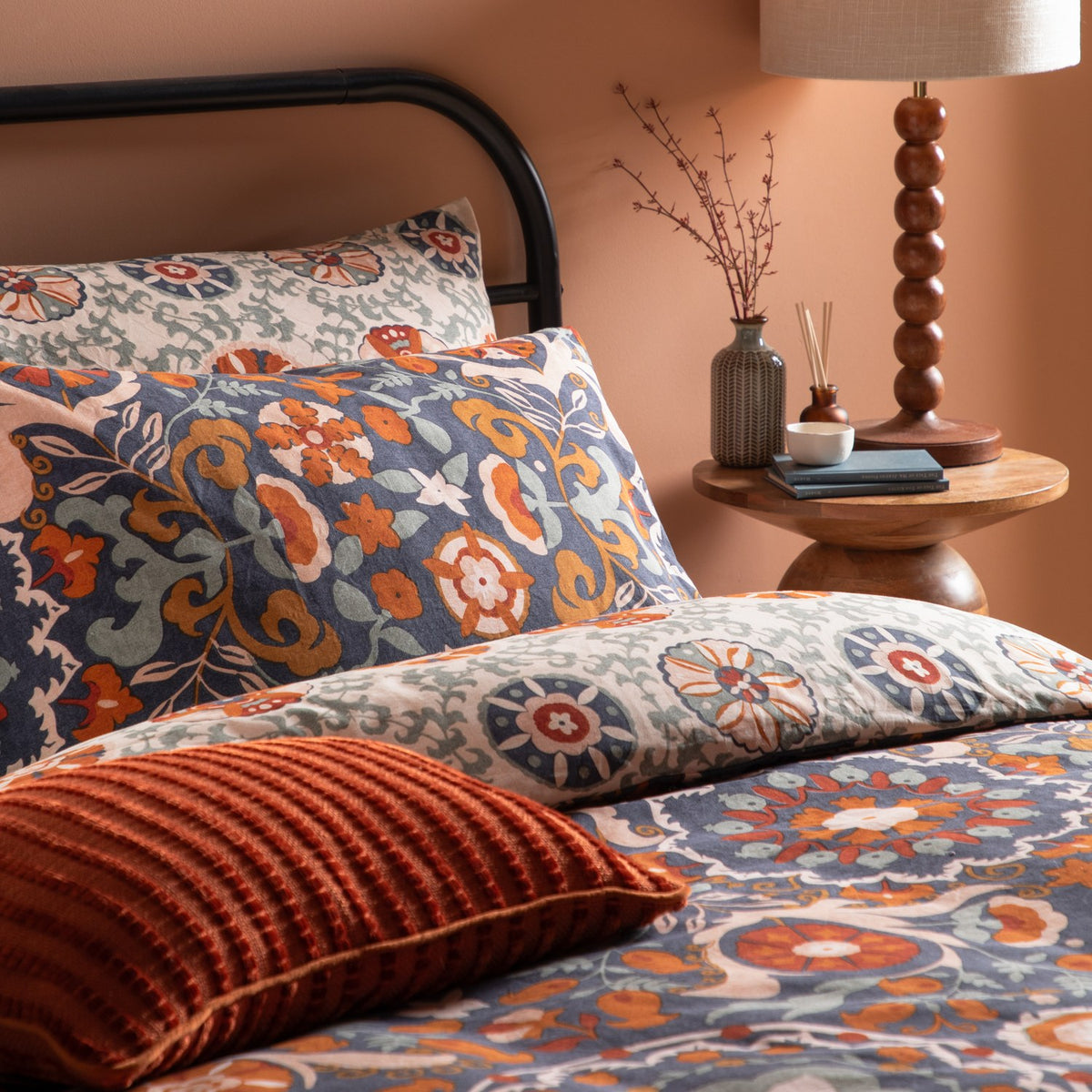 Kinfolk Reversible Floral Duvet Cover Set in denim blue with rust, orange and cream floral medallion pattern, styled on a bed with matching pillowcases and a rust cushion.