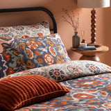 Kinfolk Reversible Floral Duvet Cover Set in denim blue with rust, orange and cream floral medallion pattern, styled on a bed with matching pillowcases and a rust cushion.
