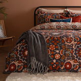 Kinfolk Reversible Floral Duvet Cover Set in denim blue with rust, orange and cream medallion pattern, styled on a bed with grey throw and cushions in a bedroom setting.