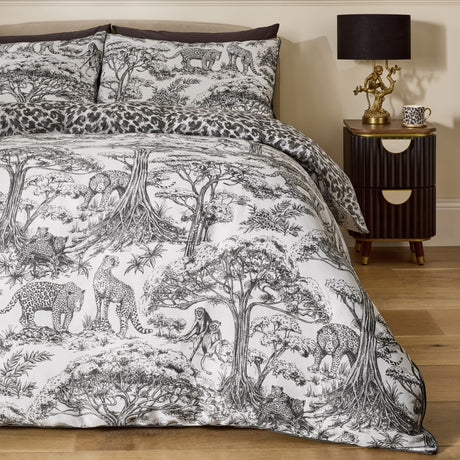 Monochrome Kisumu Cotton Jungle Duvet Cover Set on a bedroom bed, with black and white toile print of trees, leopards and monkeys, leopard-print reverse edge, and matching pillowcases.
