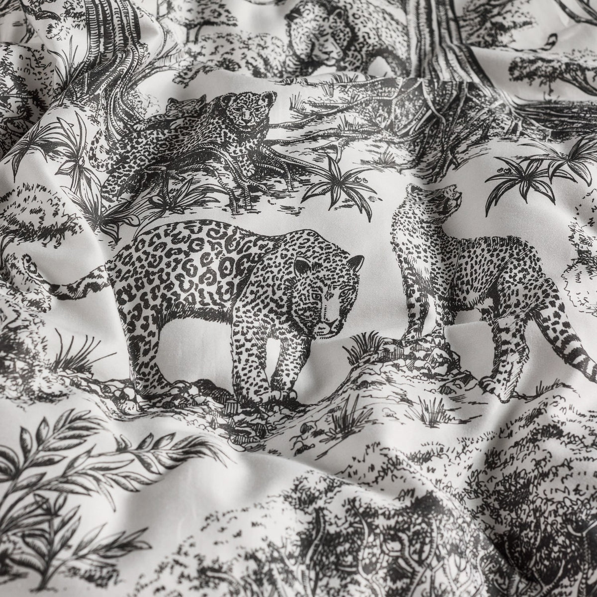 Kisumu Cotton Jungle Duvet Cover in monochrome, close-up of the crumpled cotton fabric showing black and white toile print with leopards and foliage detail.
