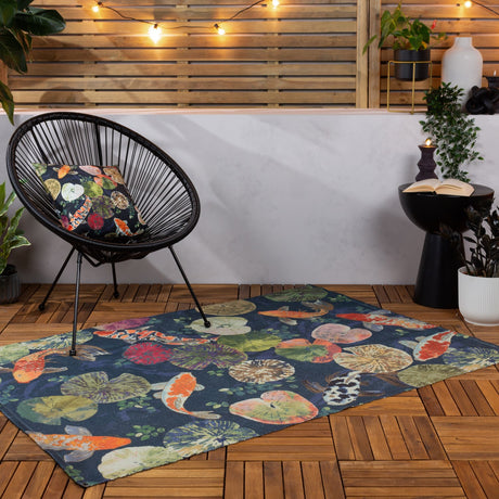 Koi Pond Animal Polyester Rug in midnight blue with orange and white koi carp and lily pad print, laid on a wooden deck beside a black rattan chair.