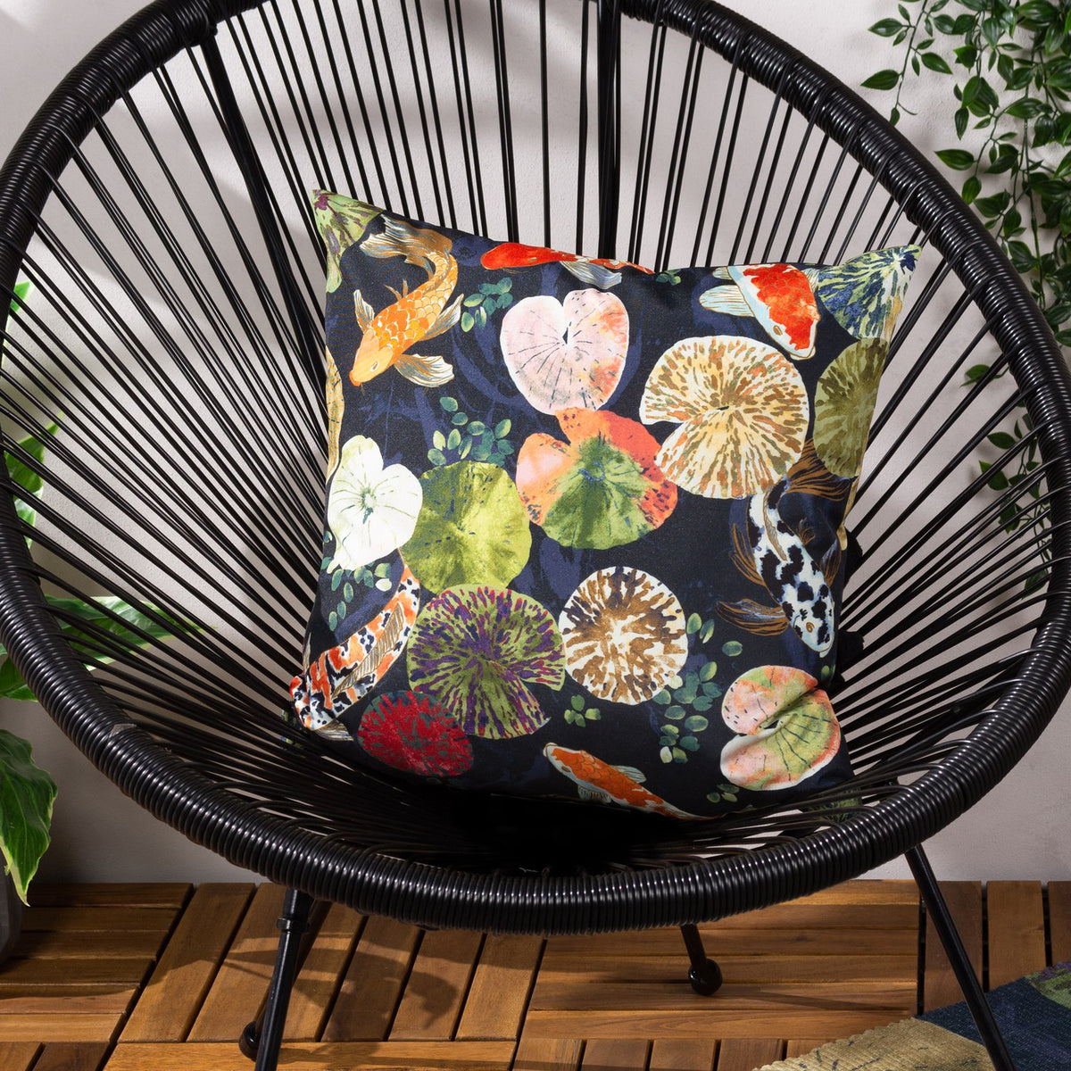 Koi Pond Reversible Polyester Cushion in Midnight, square scatter cushion with koi carp and lily pad print on black woven wicker chair.