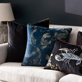 Navy velvet Koi Pond cushion embroidered with gold koi carp, shown on a sofa alongside black velvet and lobster-embroidered cushions.