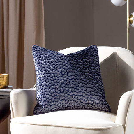 Lanzo Abstract Velvet Cushion in Dusk blue with raised circular pattern, shown on a cream armchair in a living room setting.