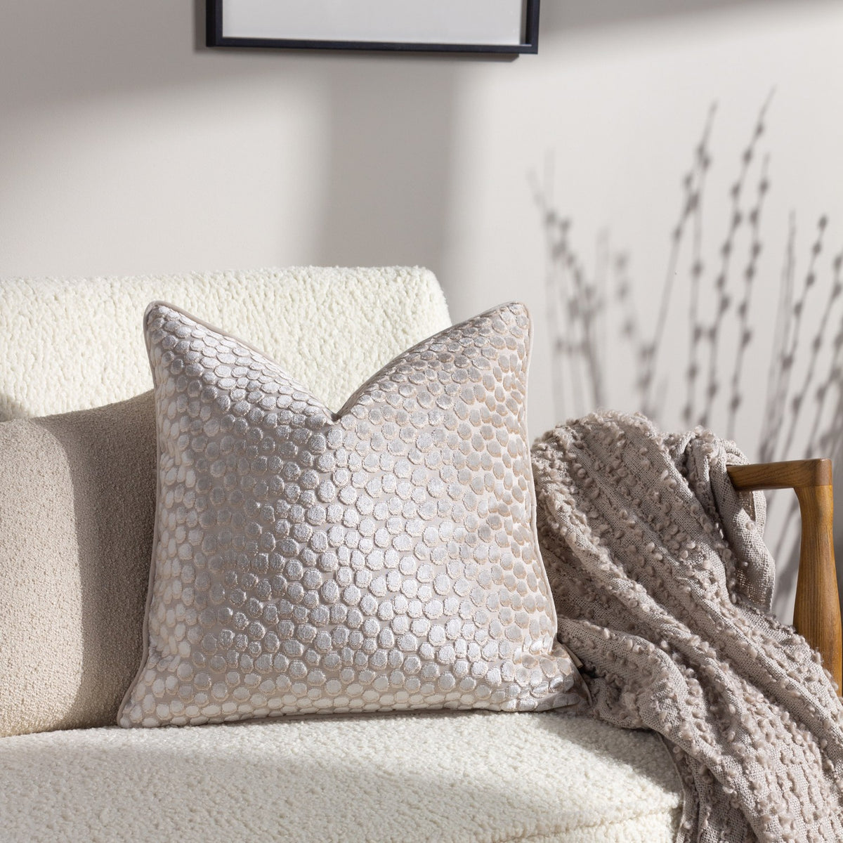 Lanzo Abstract Velvet Cushion in Moonbeam, a cream-toned square cushion with a dotted cut-velvet texture, shown on a cream boucle sofa beside a woven throw.