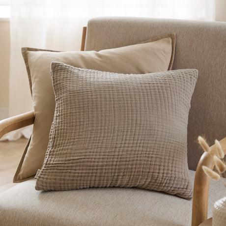 Lark Plain Cotton Cushion in mole brown, a square textured muslin cushion with rippled cotton surface, shown on a beige armchair beside another neutral cushion.