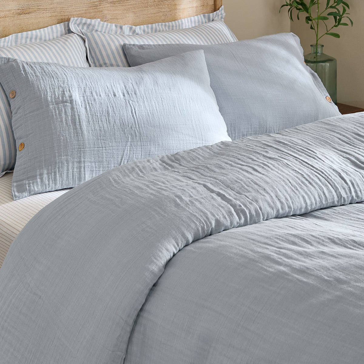 Lark Cotton Plain Duvet Cover Set in Mineral Blue on a bed, showing crinkled double-layer muslin cotton with a matching pillowcase and buttoned sham.
