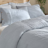Lark Cotton Plain Duvet Cover Set in Mineral Blue on a bed, showing crinkled double-layer muslin cotton with a matching pillowcase and buttoned sham.